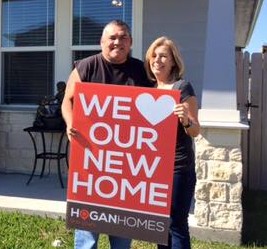 Man and woman standing outside their home and holding a sign saying "We love our new home"